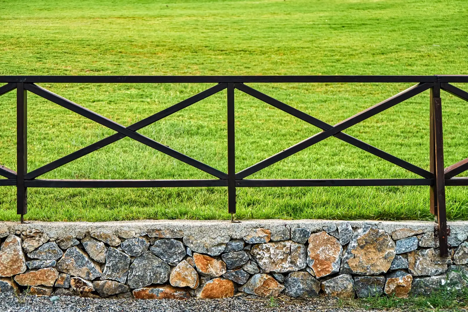Wooden rail fence standing on a low stone retaining wall beside a lawn
